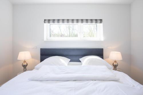 ein weißes Bett mit weißer Bettwäsche und zwei Lampen in der Unterkunft Hannes Huis in Neukirchen