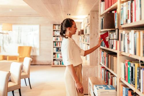 a woman is picking a book from a library shelf at Hotel Hochschober in Turracher Hohe