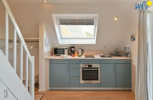 a kitchen with blue cabinets and a sink and a window at Bootshaus in den Duenen - 4 "Ferienwohnung Duenenkoje" in Wangerooge