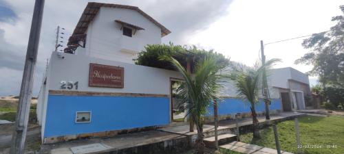 a white and blue building with palm trees in front at Hospedaria Cumbuco - Kitnets Completas in Caucaia
