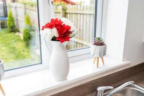 a white vase with red and white flowers on a window sill at Modern House with Parking and Garden in Doncaster