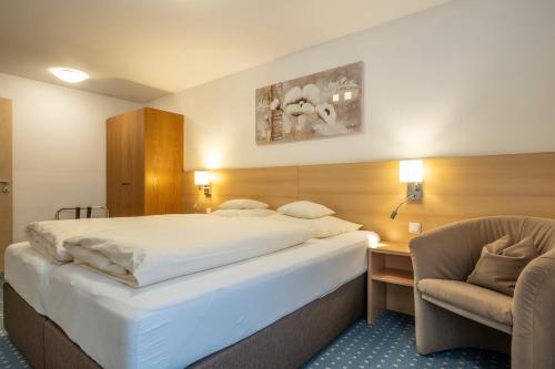 a hotel room with a large bed and a chair at Hotel-Pension Falkensteiner in Sankt Gilgen