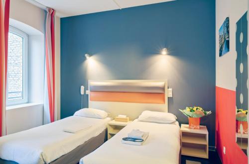 two beds in a room with a blue wall at Adonis Hotel Strasbourg in Strasbourg