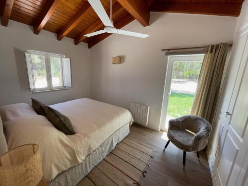 um quarto com uma cama, uma cadeira e uma janela em Monte dos Pinheiros em São Teotónio