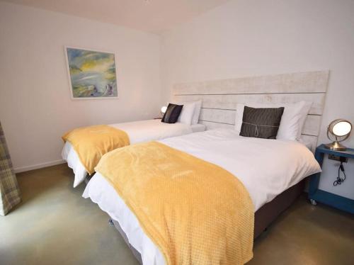two beds in a white room with yellow blankets at Ochre Cottage in Holsworthy