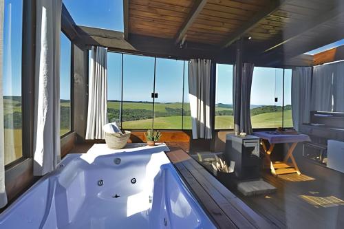 Chalé Vista do Vale في كامبارا: حوض استحمام في غرفة مع نوافذ كبيرة