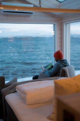 a man sitting in a chair looking out a window at the ocean at Norwegian Wild in Vangsvik