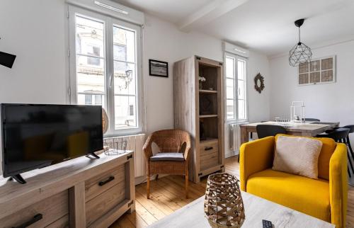 uma sala de estar com uma televisão de ecrã plano e uma cadeira amarela em Le Gardelle - Jolie maison de ville (2 chambres) em Saint Malo