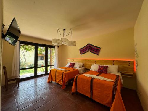 a bedroom with two beds with orange sheets and a tv at Hotel Panajachel Oasis in Panajachel