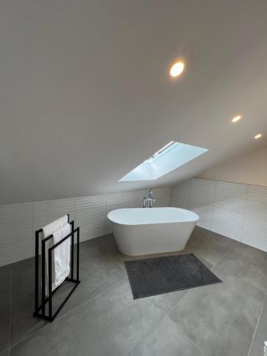 een badkamer met een wit bad en een dakraam bij Wunderschöne DHH am Tor zum Allgäu in Primisweiler