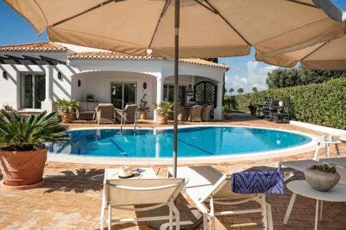 a swimming pool with chairs and an umbrella at Casa Rosella in Carvoeiro