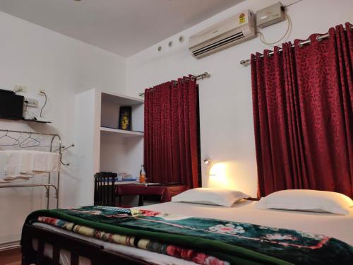 1 dormitorio con 1 cama con cortinas rojas y mesa en Kuttickattil Gardens Homestay, en Kottayam