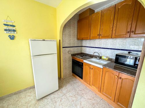 eine Küche mit einem weißen Kühlschrank und Holzschränken in der Unterkunft Apartamentos Costa Azahar 3000 in Alcossebre