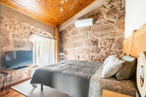 a bedroom with a stone wall with a bed and a television at Segredos da Montanha - Mangualde in Mangualde