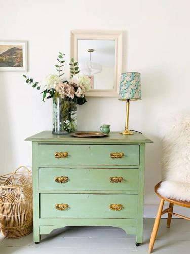a green dresser with a vase of flowers on it at The Yellow cottage on the hill. in Framlingham