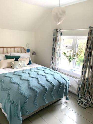 a bedroom with a bed with a blue blanket and a window at The Yellow cottage on the hill. in Framlingham