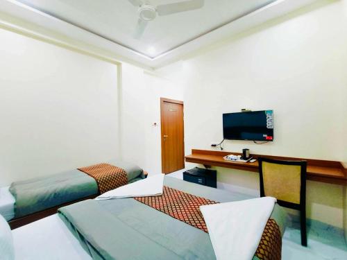 a room with two beds and a desk and a television at Hotel Sai Sneha in Shirdi