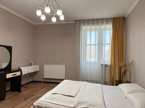 1 dormitorio con cama, escritorio y ventana en Уютная рядом с парком, en Uralsk