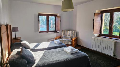 a bedroom with two beds and a chair and windows at Casa de Aldea la Piniella in Villahormes