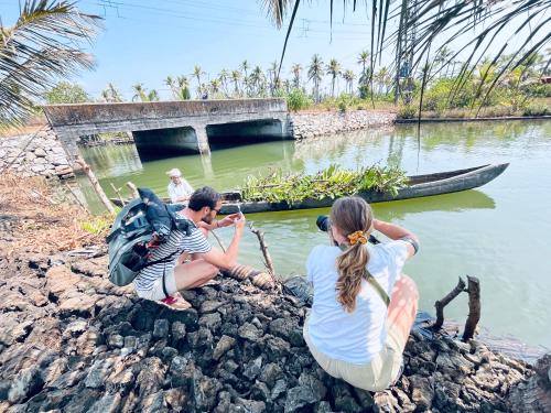 a group of people sitting on the rocks near the water at Riverrootsstays in Munroe Island