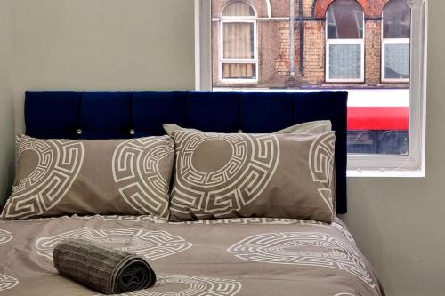 2 Bed Cosy Flat close to Bus & Tube Station في لندن: سرير مع اللوح الأمامي الأزرق وبعض الوسائد