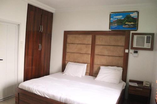 - une chambre avec un lit blanc et une tête de lit en bois dans l'établissement Rocket Room Hotel & Suites Limited, à Port Harcourt