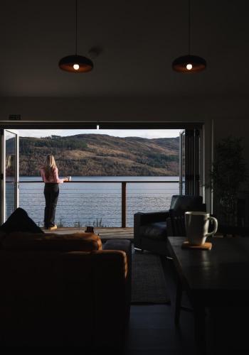 a woman standing in a living room looking out at the water at Shoreland Lodges - Cherry Lodge in Fort Augustus