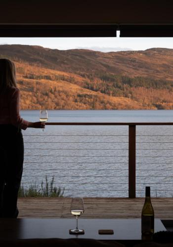 a woman holding two glasses of wine overlooking a lake at Shoreland Lodges - Cherry Lodge in Fort Augustus