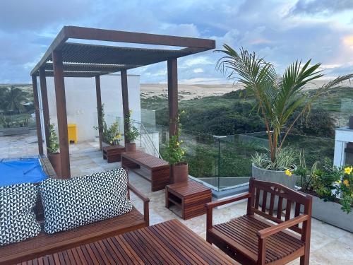 a patio with wooden benches and a gazebo at Apartamento Chique frente ao mar in Flecheiras