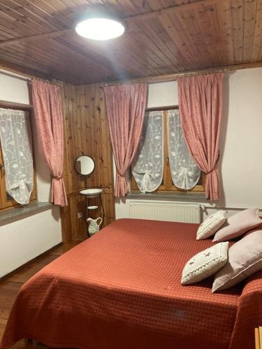 a bedroom with a bed with red sheets and windows at Monica in Santo Stefano di Cadore