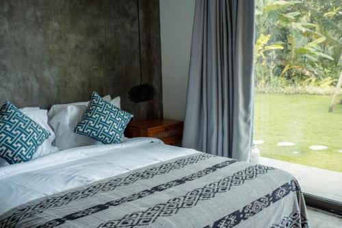 a bed with blue and white pillows and a window at Hatiku Di Bali - Ubud in Tegalalang
