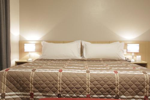 a bedroom with a large bed with two lamps at Castelo Inn Hotel in Goiânia