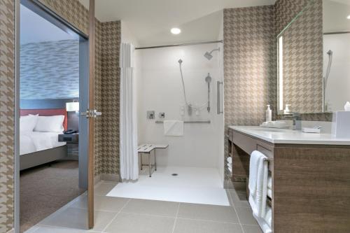 a bathroom with a shower and a sink and a bed at Home2 Suites By Hilton Tulsa Airport in Tulsa