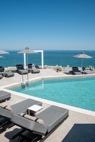 a swimming pool with chairs and umbrellas next to the ocean at Akrotiri Olympus Luxury Suites - Adults Only in Plaka Litochorou