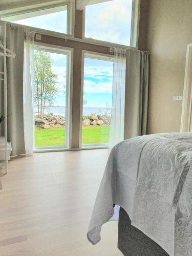a bedroom with a bed and two large windows at Stuga med havsutsikt in Robertsfors