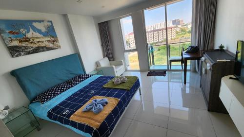 Schlafzimmer mit einem blauen Bett, einem Schreibtisch und Fenstern in der Unterkunft City Center Residence Pattaya in Pattaya