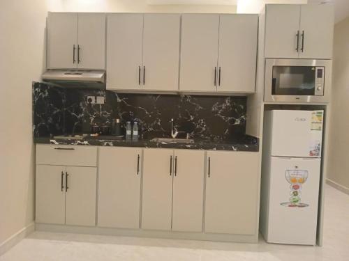 a kitchen with white cabinets and a microwave and a refrigerator at فندق دره الراشد للشقق المخدومه in Riyadh