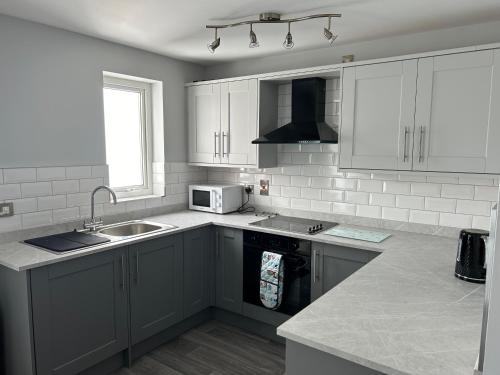 a kitchen with white cabinets and a sink and a microwave at Seaside Marine First Floor Apartment in Ballycastle