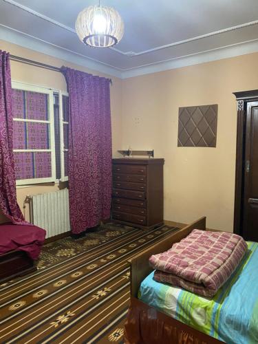 Schlafzimmer mit einem Bett, einer Kommode und lila Vorhängen in der Unterkunft Rue Mohamed khoudi El Biar in Ben ʼAknoûn