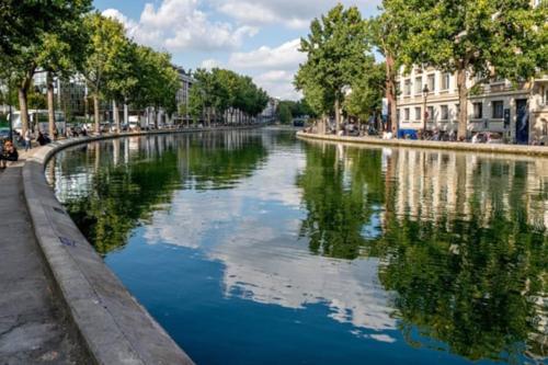 un río con reflejos de edificios y árboles en el agua en Cosy appartement - La Villette, en París