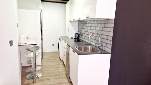 una cocina con fregadero de acero inoxidable y armarios blancos en Homelike Malasaña, en Madrid