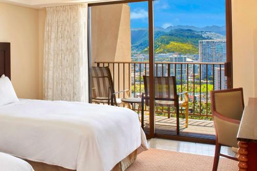 a bedroom with a bed and a balcony with chairs at Hilton Hawaiian Village Waikiki Beach Resort in Honolulu