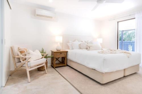 a white bedroom with a bed and a chair at Coolum Family Hideaway - Private Pool & Sauna in Coolum Beach