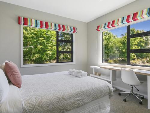 a bedroom with a bed and a desk and two windows at Lake Taupō Luxury Views in Taupo