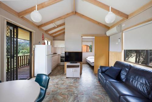 a living room with a black leather couch and a kitchen at Reflections Grabine Lakeside - Holiday Park in Bigga