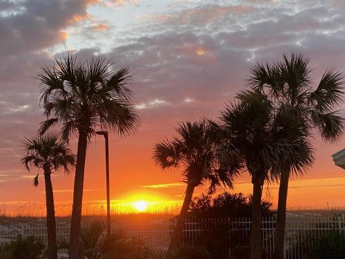 a sunset with palm trees in front of a fence at Your Beach Therapy Awaits at Sans Souci in Pensacola Beach