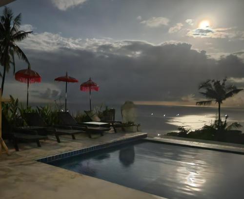a swimming pool with chairs and umbrellas and the ocean at Villa Umbrella in Senggigi 