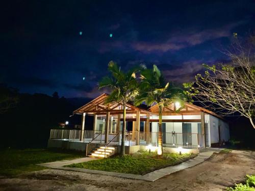 una casa con porche y palmeras por la noche en Pousada Rural Recanto do Lago, en Pedra Azul