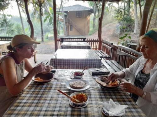 Duas mulheres sentadas à mesa a comer comida. em Morakanda Eco Villa em Elpitiya