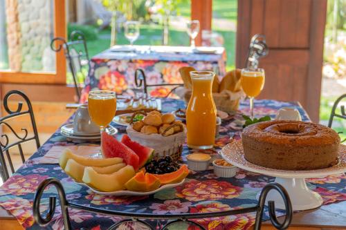 a table with a cake and fruit and orange juice at Pousada Chalés Jardim das Bromélias - Visconde de Mauá in Visconde De Maua